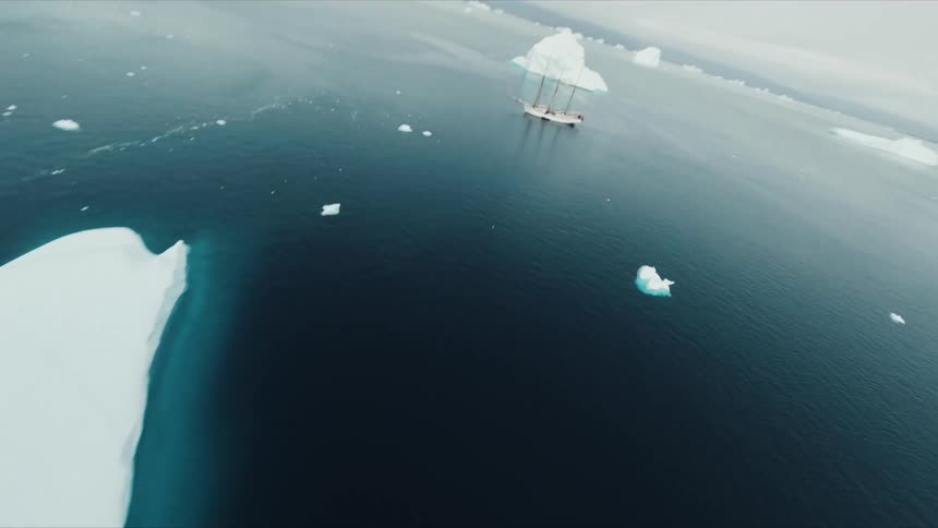 Sailing ship floats in open water between icebergs and sea ice on an overcast day