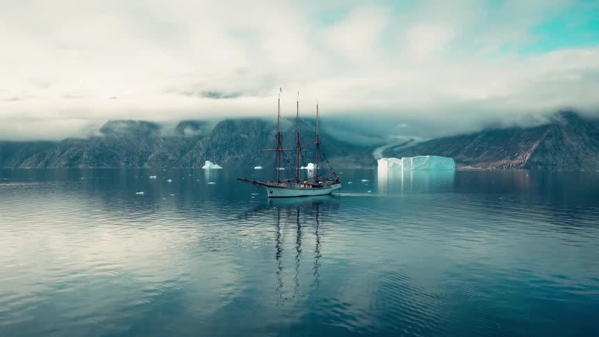 A three masted sailing ship navigates through calm arctic waters surrounded by icebergs and mist covered mountains