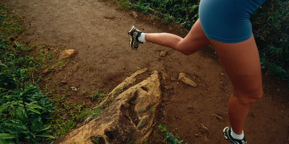 Woman leaps over a rock as she runs on a trail in the woods