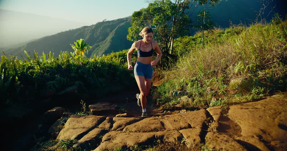 A woman is jogging on a rocky trail in the mountains