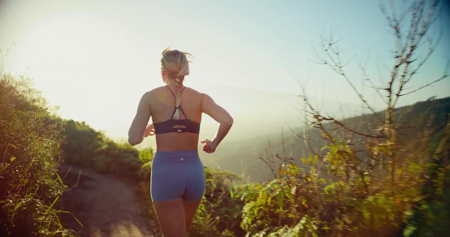 Woman stands looking at the landscape and runs on a trail along the edge of the mountain