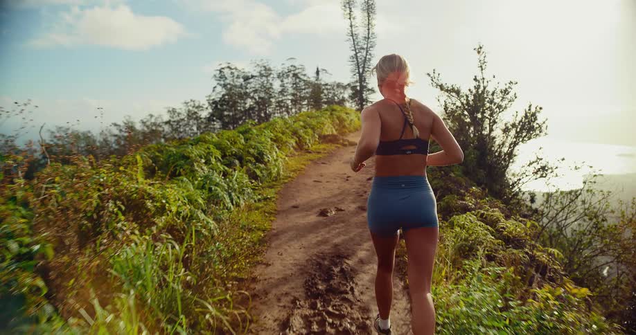 Woman runs on a trail along the edge of the mountain