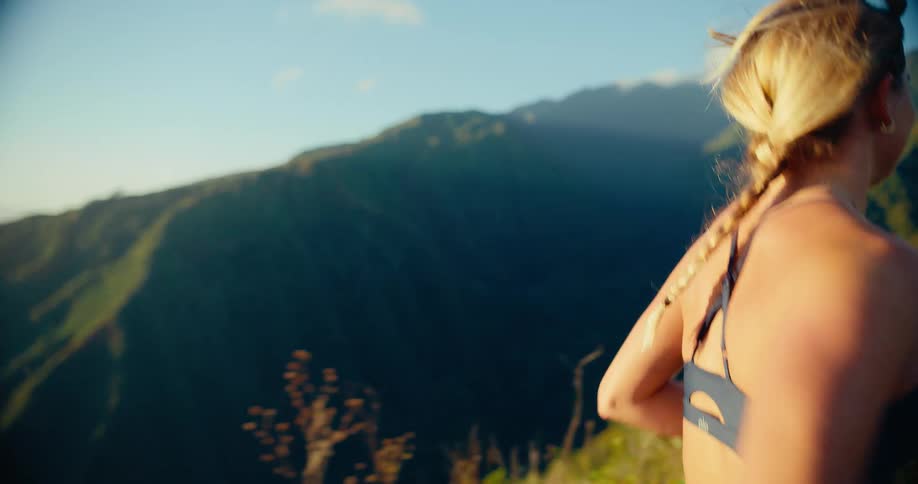 Woman swings her arms as she runs on a trail at the edge of a mountain