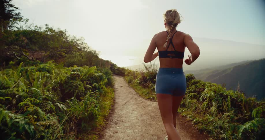 A woman is jogging on a trail on the side of a mountain
