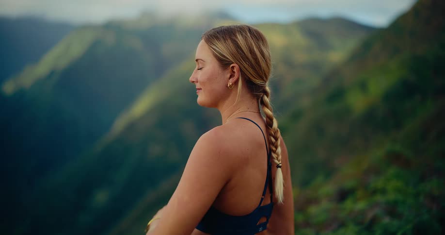 Woman stands at the edge of a mountain as she holds her arms and stretches