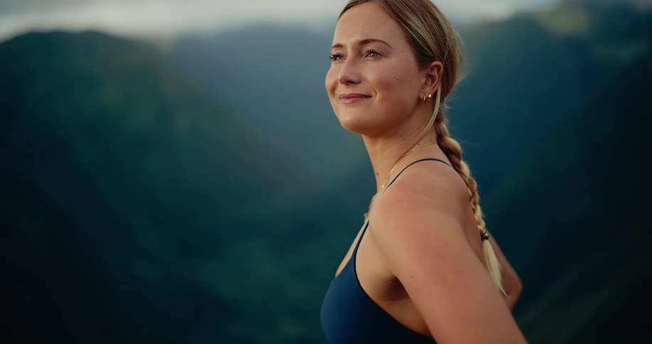 The woman turns her head to look out over the vast green mountain valley with a serene smileas the camera circles around her she closes her eyes briefly appearing to soak in the peaceful landscape