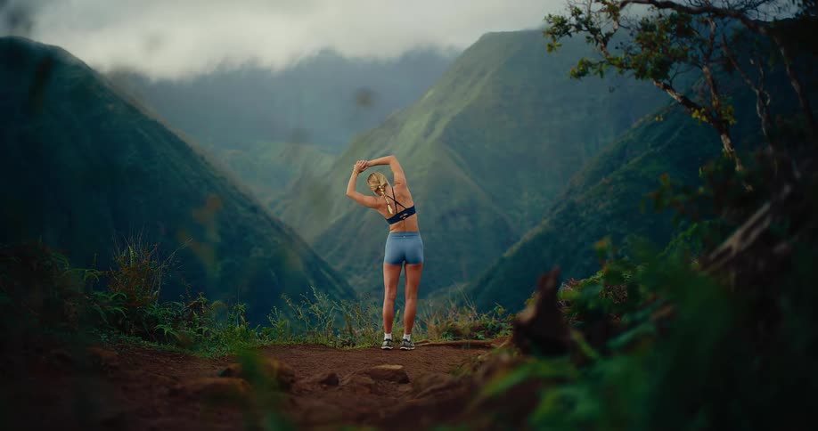 A woman is stopped on a trail in the mountains as she stretches