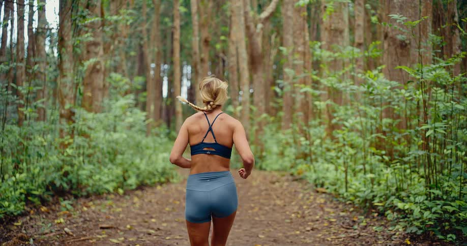 Woman swings her arms as she runs on a trail into the forest