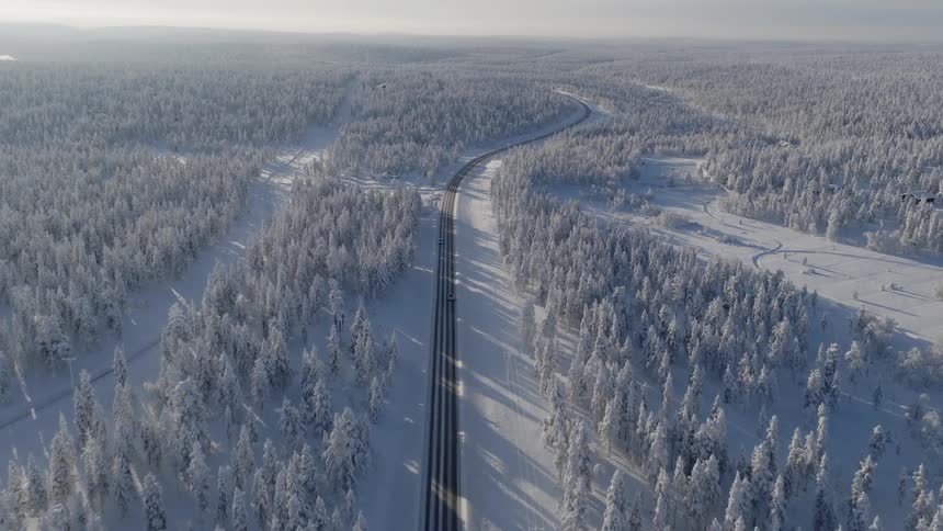 Vehicles move along a mostlye empty road passing through the forest on a winter day