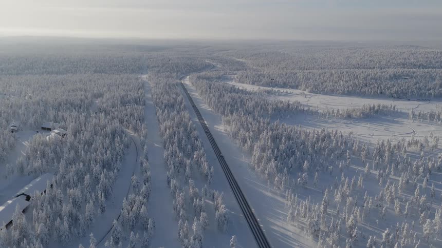 Few vehicles travel along a highway passing a frost covered forest near a small town on a cloudy winter day