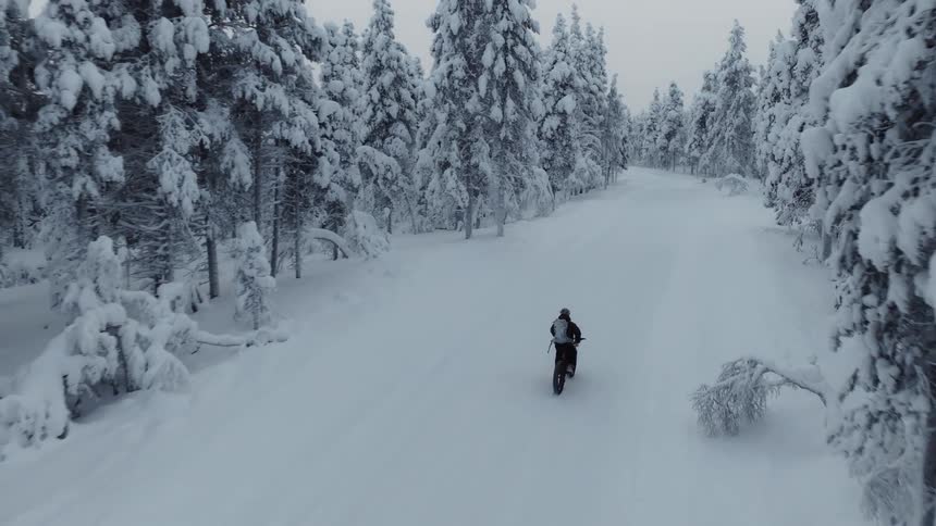 Man riding a bicycle on a snow covered road through the forest