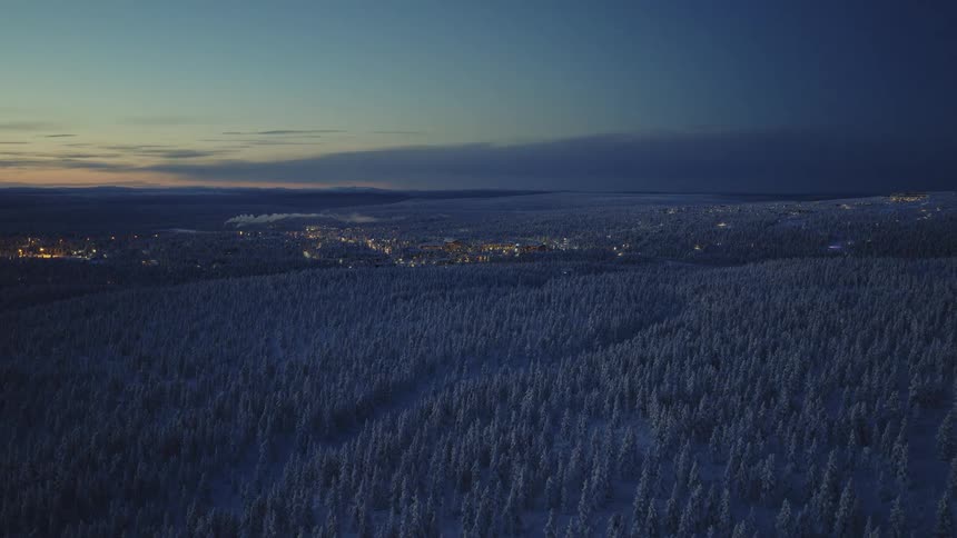 A sprawling forest is covered in snow as the sun is set below the horizon