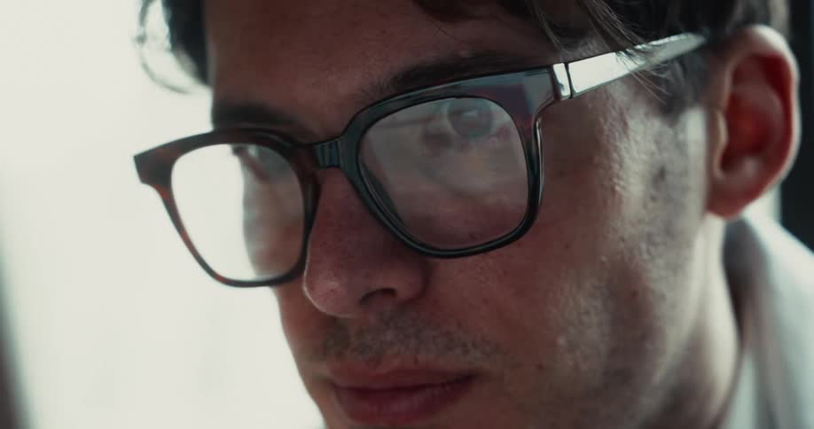 An up close viewof a man looking atan item close to has face with reflections in his eyeglasses possibly a computer