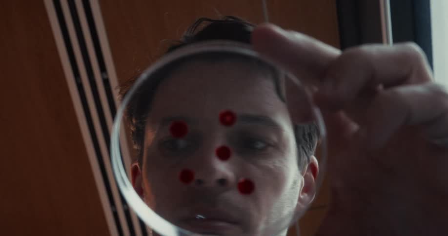 A man drops red liquid from a pipette onto a glass dish while looking through it