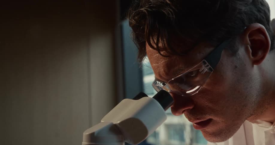 The man puts on glasses and looks through the microscope