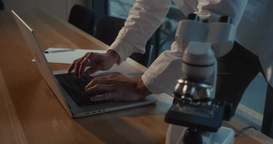 Doctor bending over a table typing on a laptop computer