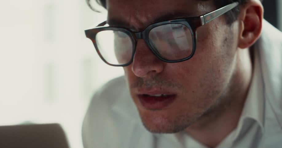 A man wearing glasses looks at a screen with a focused expression