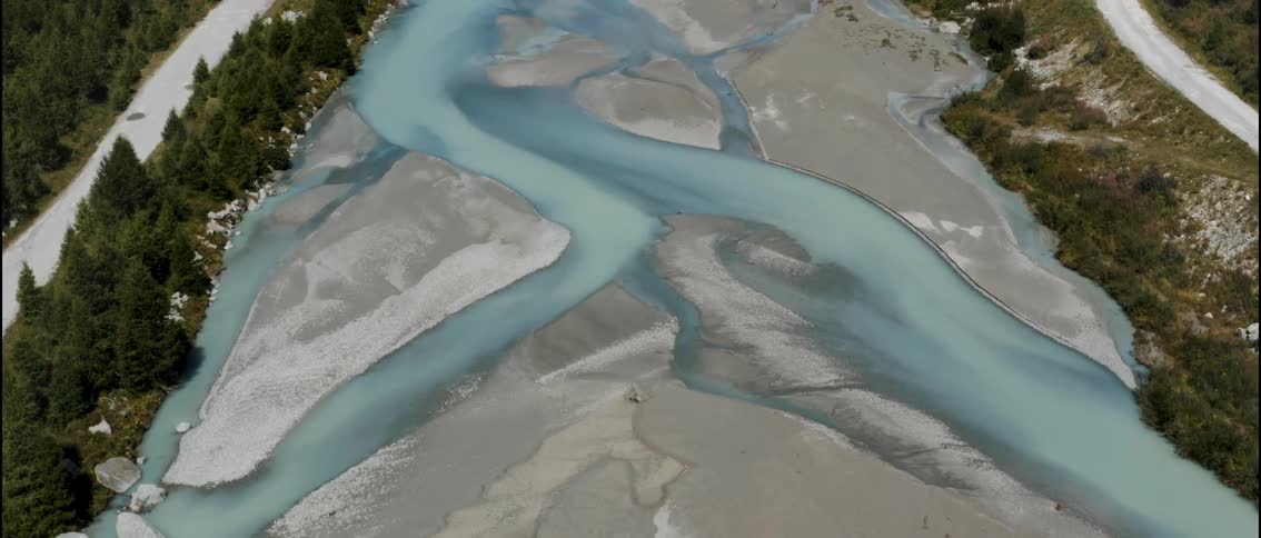 Aerial view of a bluish river forming winding channels over a gravel bed between forested areas