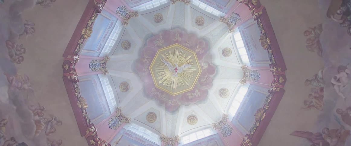 A view looking up at an ornate octagonal ceiling dome with pink and gold decorations and light streaming through several high windows