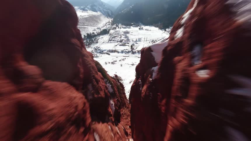 An fpv drone flies rapidly over a snow covered mountain ridge and dives through a narrow red rock canyon