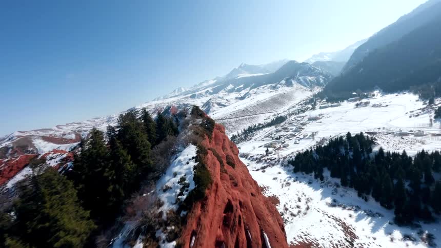 Red rock cliff with trees on top and snowcovered mountains in the background