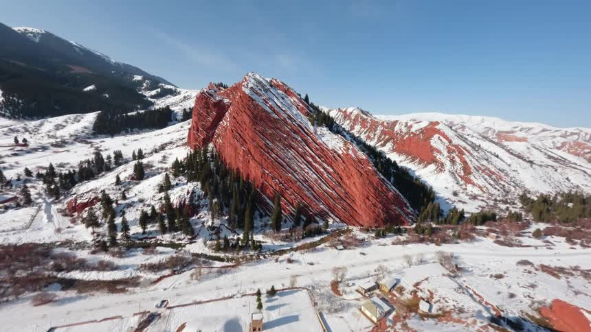 A striking red rock formation amidst a snowcovered mountainous landscape under a clear blue sky