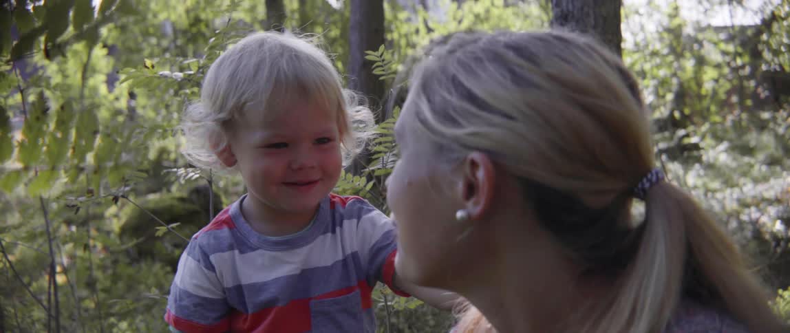 Toddler boy smiling big as his mother talks to him outside in nature