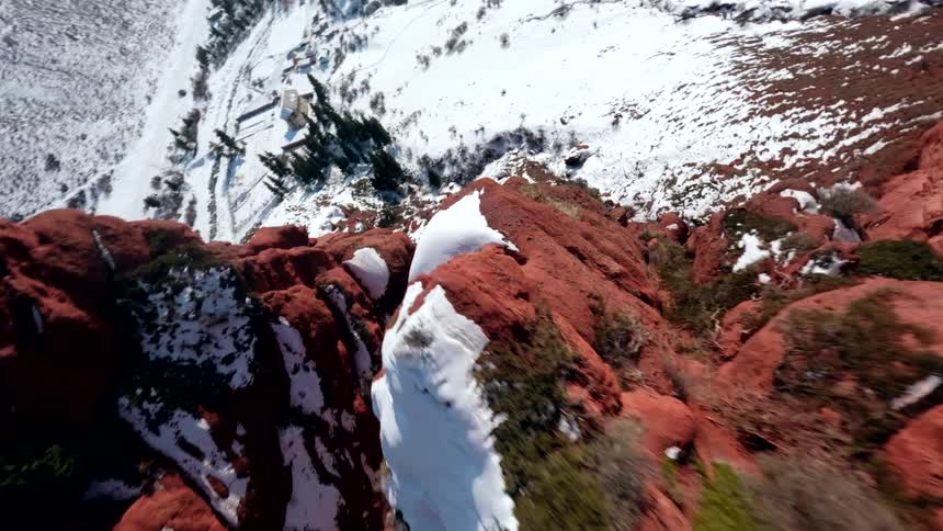 A rapidly twisting aerial view of a red rocky mountain range coated with snow