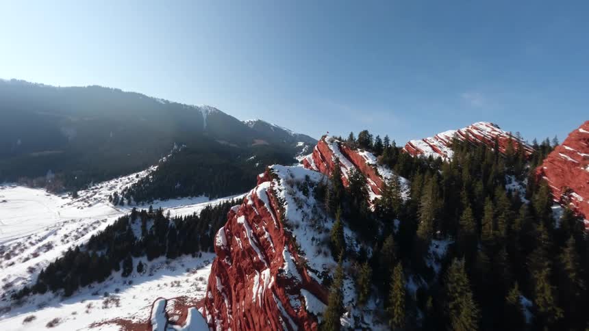 Aerial view of trees on a red rock mountain ridge with snow