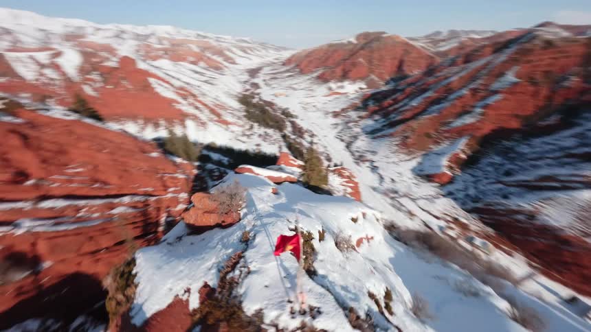 Red flag raised on a snowcovered cliff overlooking reddish mountains