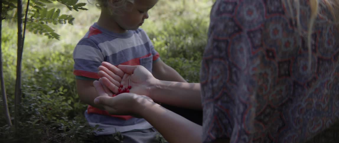 Woman talking with a child while they work in a field with berries in her hands