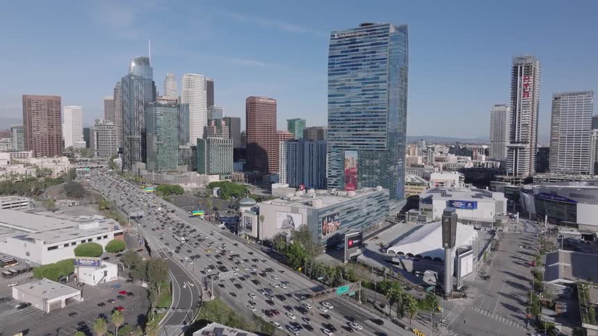 An aerial view shows heavy vehicle traffic on a multi lane freeway passing through downtown Los Angeles with tall skyscrapers