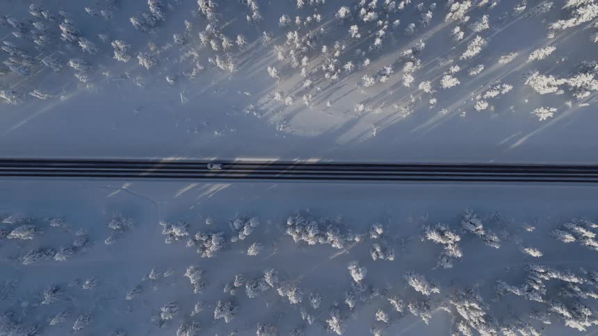 Aerial view of a truck traveling on a road through a snow covered forest