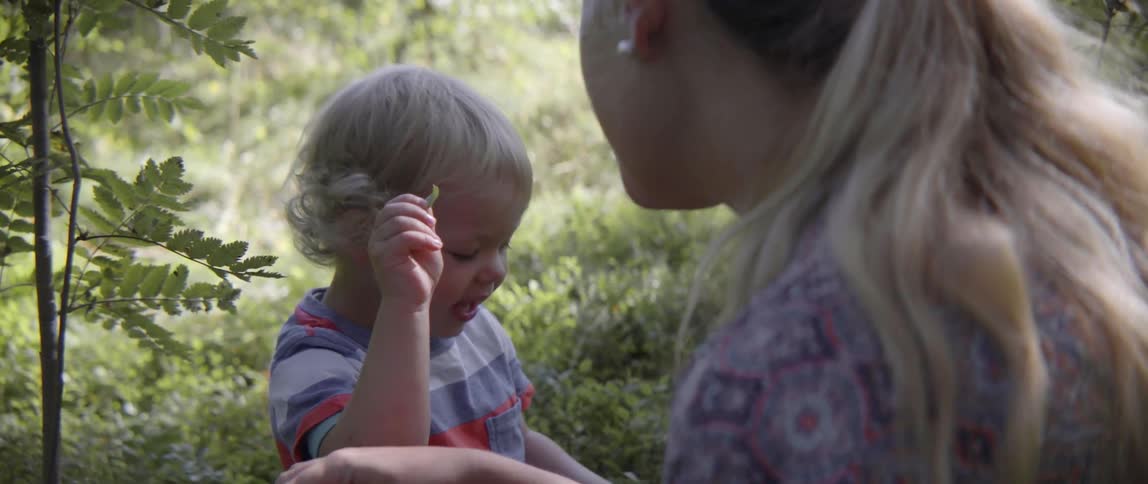 A woman and young boy sit together in a lush green grassy field outdoors.