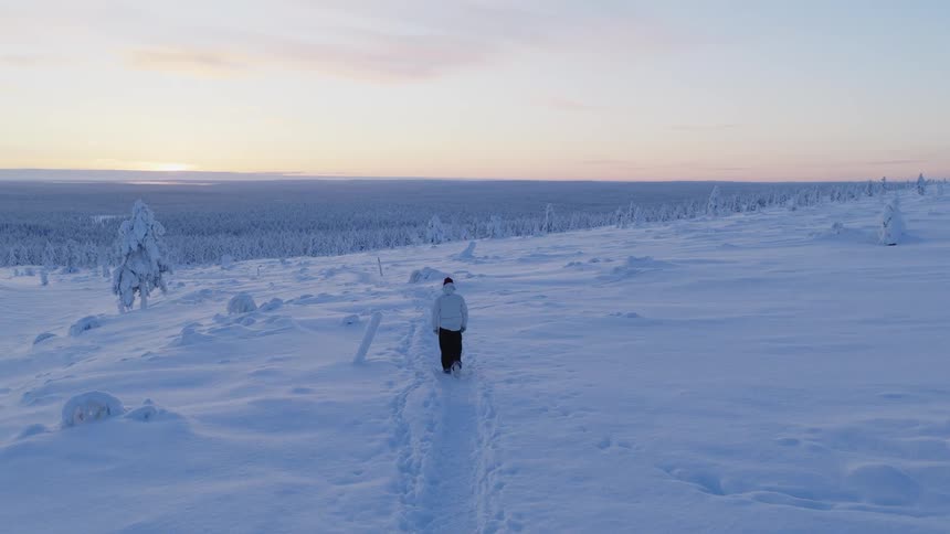 A man walking along a snowy mountain path at midday