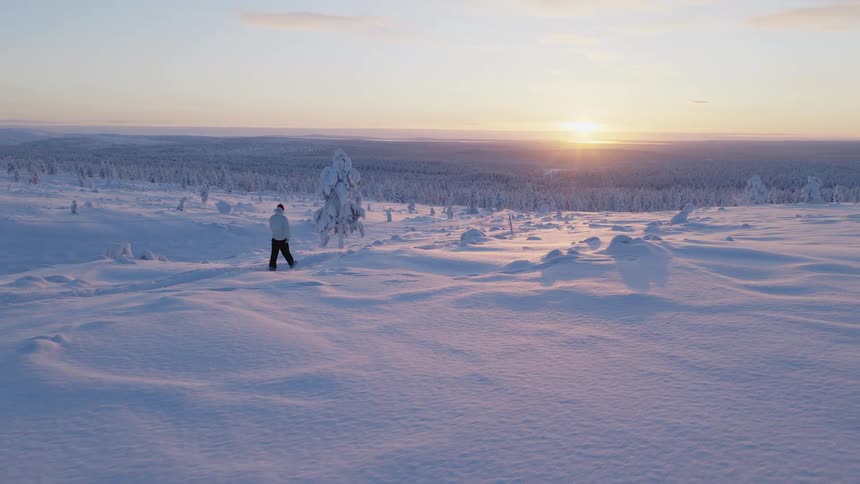 Person walking on a mountain path in the snow with a forest in the valley