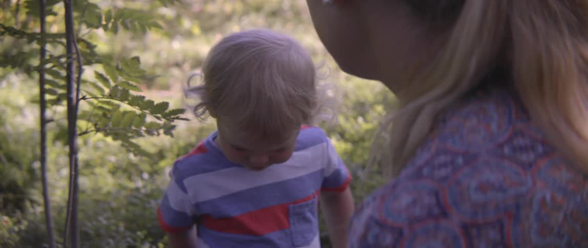 A woman shows a handful of fresh red berries to a young toddler boy.