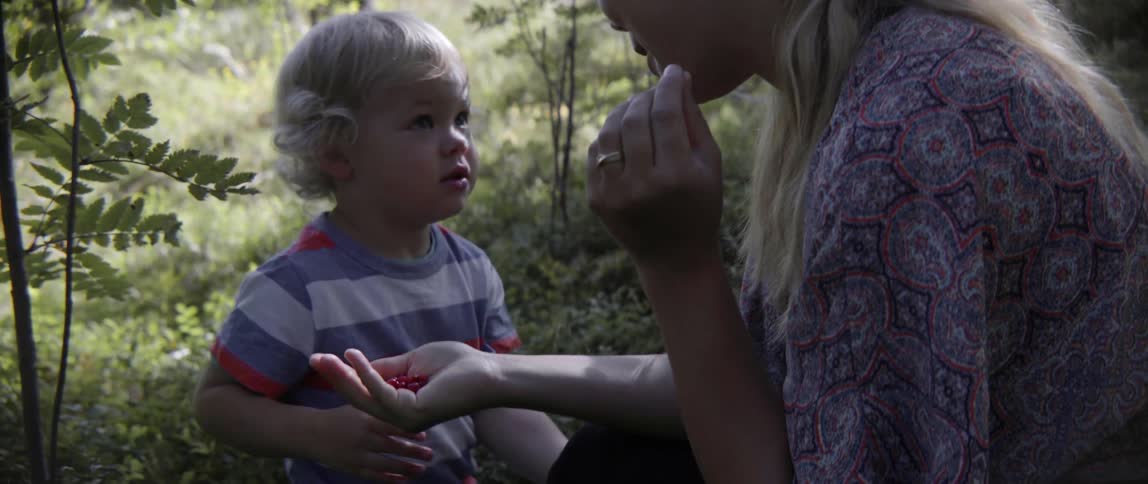A woman is offering her toddler child some berries as they sit outside