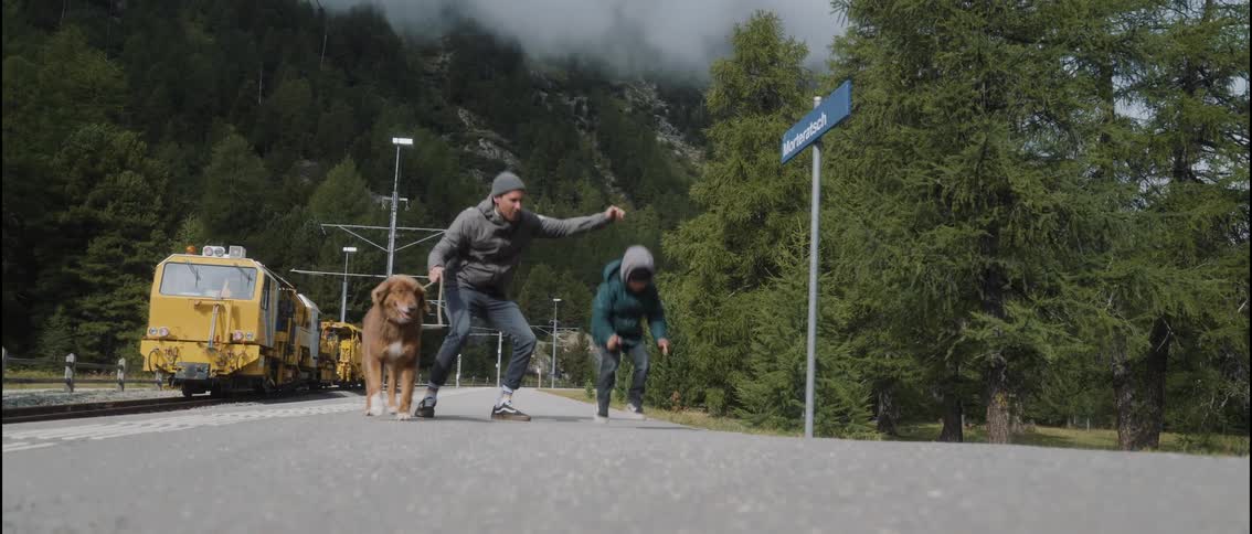 Father and son dance while on a highway near a parked train as low lying clouds cover the forest in the background