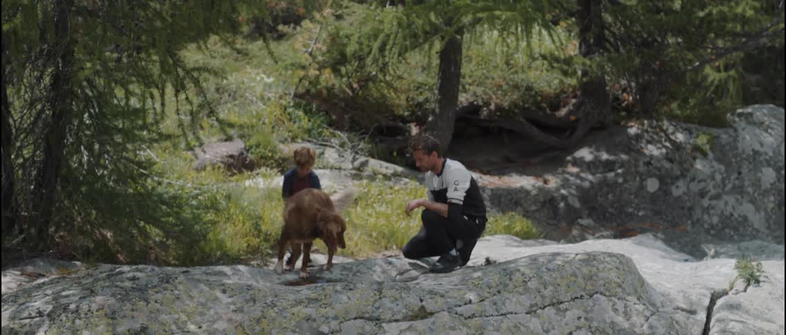 Man and his young son playing with their dog on rocks outside of the forest
