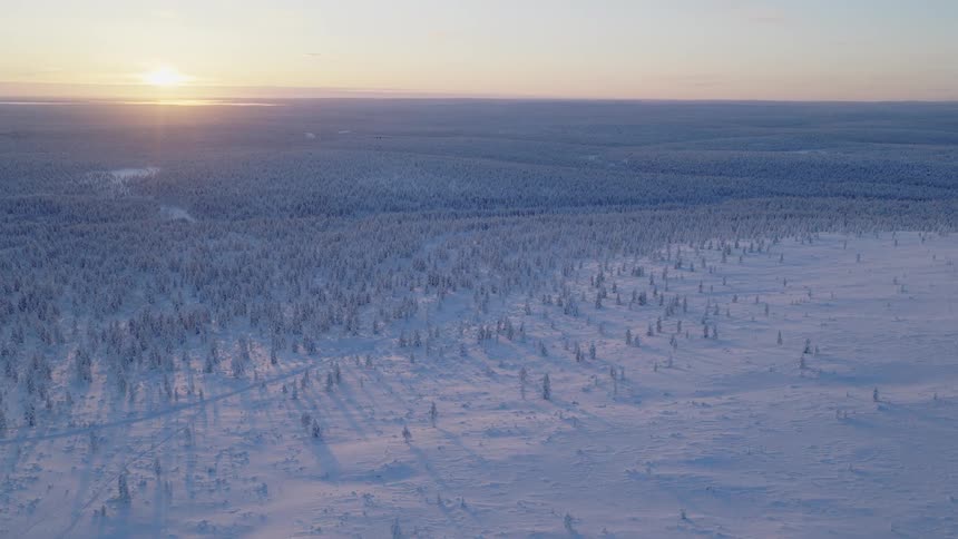 Aerial view of snow covering the mountain and trees in the forest across the landscape as the sun shines on the horizon