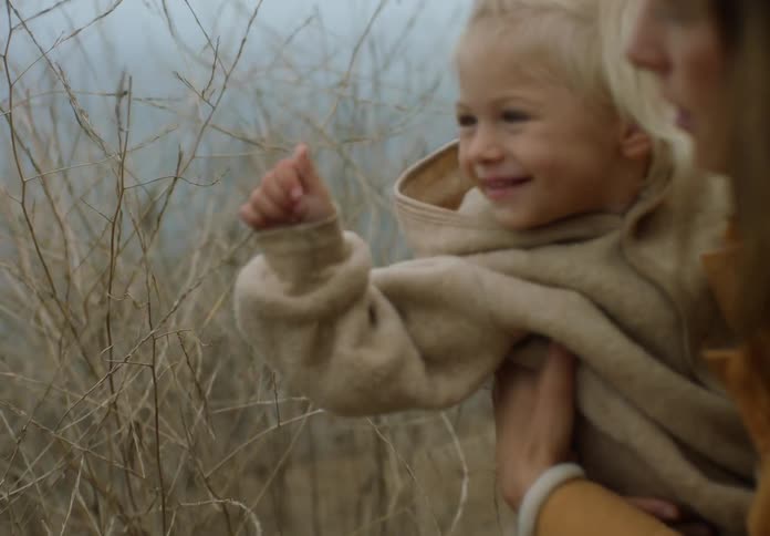 A woman holds a young girl who is happy to touch a plant