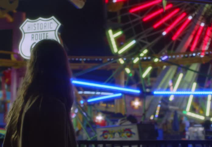 Woman walks past an amusement park ride while at the amusement park at night