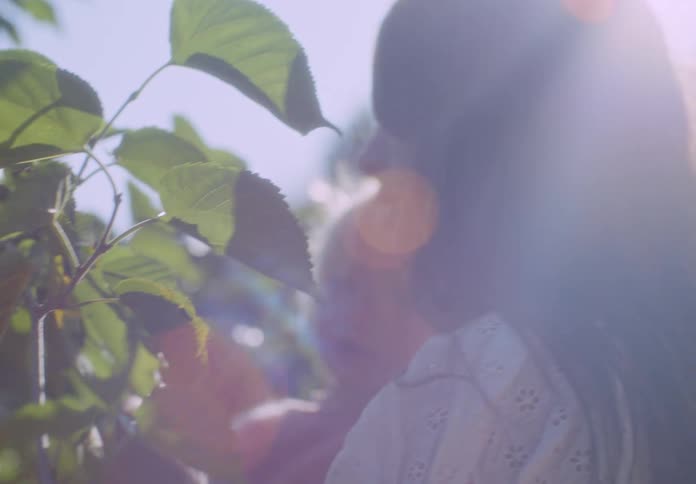 Mother holding her daughter examines a plant as she stands outdoors on a sunny summer day
