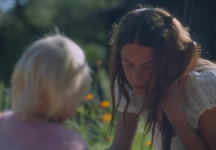 Woman holds a hairbrush while interacting with a child in a flower garden