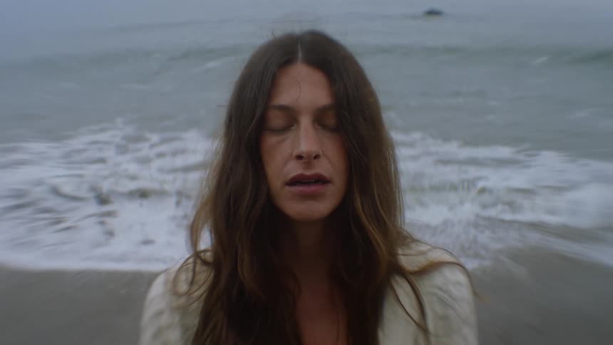 Woman on the beach takes a deep breath as the waves flow onto the beach