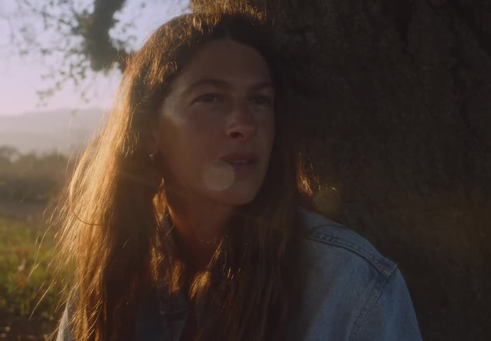 Woman sits in a field and leans against a tree while thinking on an autumn day