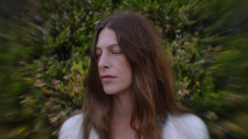 Woman stands outdoors near a bush on a windy day