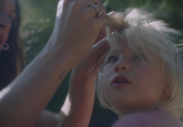 A woman attempts to style the hair of a very young girl who is looking around