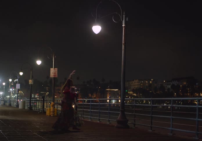 Mother holds her young daughter while dancing on the waterfront near a lamp pole at night
